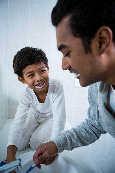 Adult and child brush their teeth together at the bathroom sink